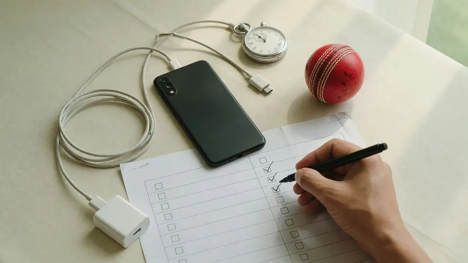Adult writing matchday testing notes beside an unbranded smartphone